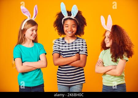 Studio Portrait Shot Of Three Children Friends Wearing Easter Rabbit Ears Against Yellow Background Stock Photo