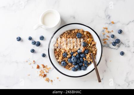 Bowl of granola with blueberries and jar of dairy free milk on white marble table background, top view Stock Photo