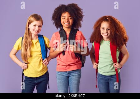 Studio Shot Of Three Children With Backpacks Going To School On Purple Background Stock Photo