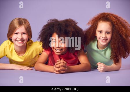 Studio Portrait Shot Of Three Children Friends Lying On Floor Against Yellow Background Stock Photo