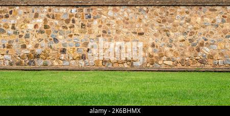 Panoramic view of the old vintage stone wall and green lawn at a garden as landscape design Stock Photo