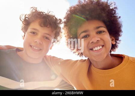 Low Angle Portrait Of Two Boys Having Fun Playing Outdoors Looking Down Into Camera With Lens Flare Stock Photo