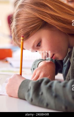Close Up Of Female Elementary School Student At Desk Writing In Book Stock Photo