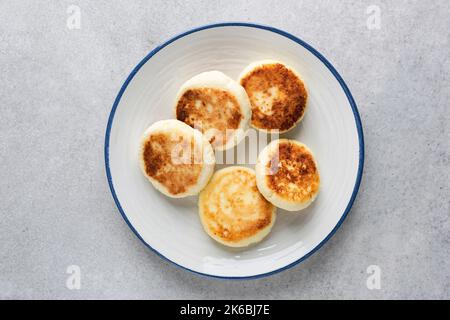 Cottage cheese fritters Syrniki on white plate, top view. Grey concrete background Stock Photo