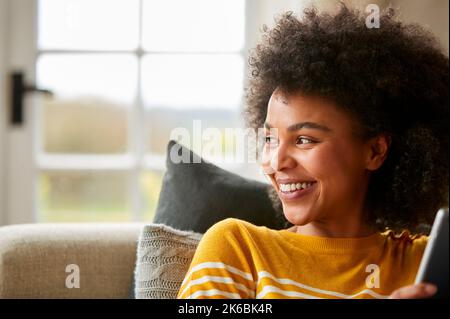 Woman Relaxing On Sofa At Home Using Digital Tablet To Stream Movie Or Shop Online Stock Photo