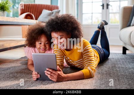 Mother And Daughter Having Fun Lying On Floor Streaming Movie On Digital Tablet At Home Together Stock Photo