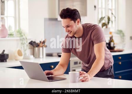 Transgender Man Working From Home Looking At Laptop On Kitchen Counter Stock Photo