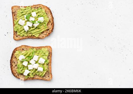 Whole grain toasted bread with mashed avocado and feta cheese on white background, top view copy space Stock Photo