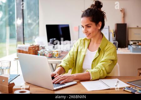 Young Woman Running Online Business From Home Selling Boutique Candles Using Laptop Stock Photo