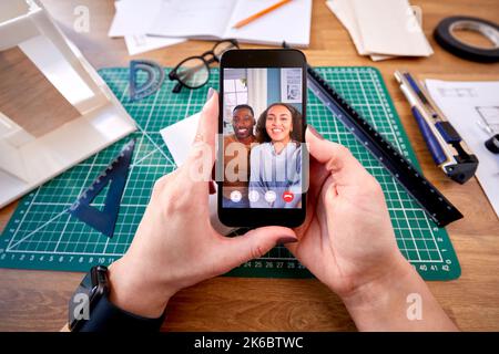 POV Shot Of Female Architect Working In Office Having Virtual Meeting With Couple On Mobile Phone Stock Photo