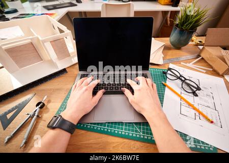 POV Shot Of Female Architect Working In Office On Plans For New Building Using Laptop Stock Photo