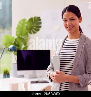Portrait Of Female Architect Standing In Office Holding Laptop Stock Photo
