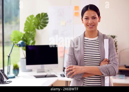 Portrait Of Female Architect Standing In Office Holding Rolled Up Building Plans Stock Photo