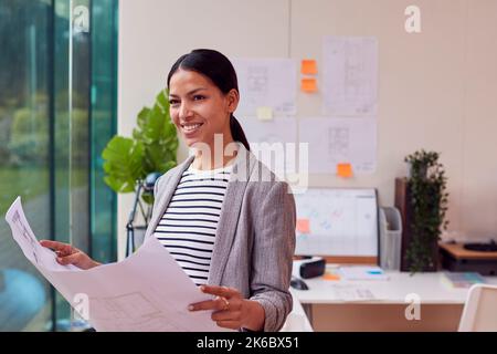 Female Architect Standing In Office Looking At Building Plans Stock Photo