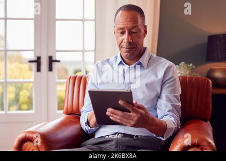 Mature Man Or Businessman Working From Home Sitting In Armchair Using Digital Tablet Stock Photo