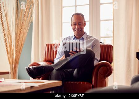 Mature Man Or Businessman Working From Home Sitting In Armchair Using Digital Tablet Stock Photo