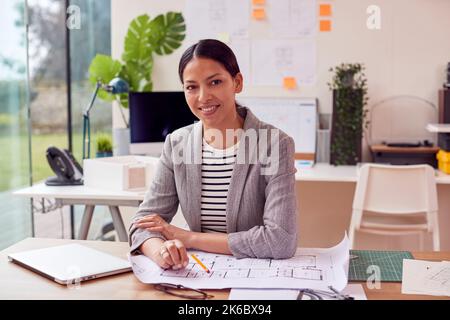 Portrait Of Female Architect Working In Office On Plans For New Building Using Laptop Stock Photo