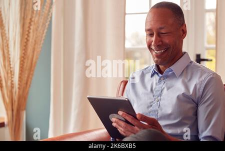 Mature Man Or Businessman Working From Home Sitting In Armchair Using Digital Tablet Stock Photo