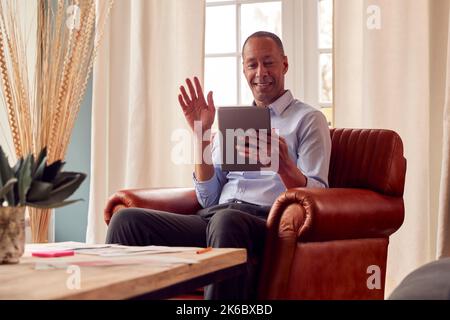 Mature Man Or Businessman Working From Home Sits In Armchair Having Video Call On Digital Tablet Stock Photo
