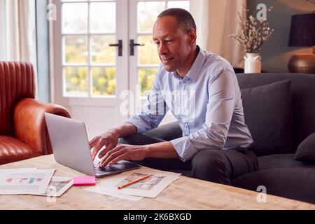 Mature Male Architect Or Interior Designer Working From Home Looking At Designs On Laptop Stock Photo