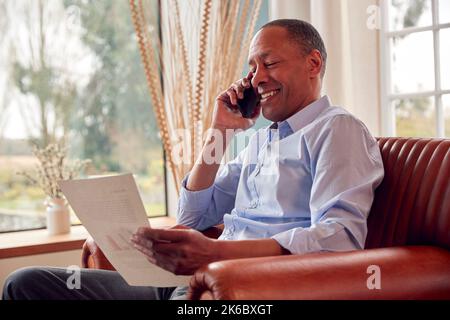 Mature Male Architect Or Interior Designer Working From Home Discussing Designs On Mobile Phone Stock Photo