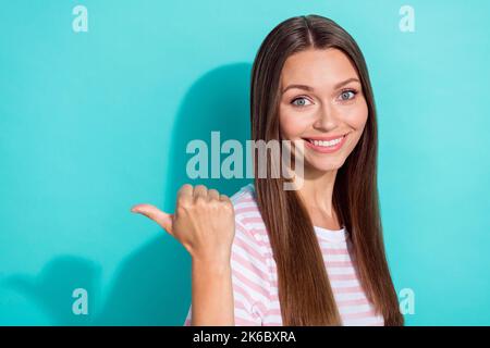 Photo of positive satisfied lovely girl straight hairdo dressed striped t-shirt directing empty space isolated on teal color background Stock Photo