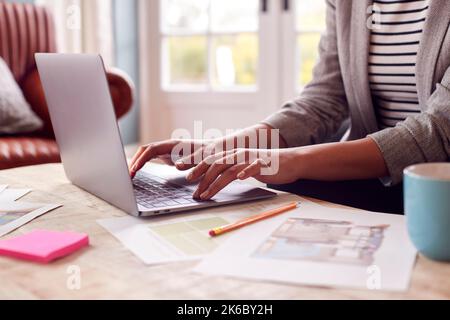 Close Up Of Female Architect Or Interior Designer Working From Home Looking At Designs On Laptop Stock Photo