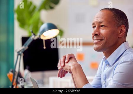 Mature Male Architect With Laptop Working In Office At Desk On Plans For New Building Stock Photo
