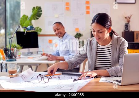 Male And Female Architects Working In Office At Desks On Plans For New Building Stock Photo