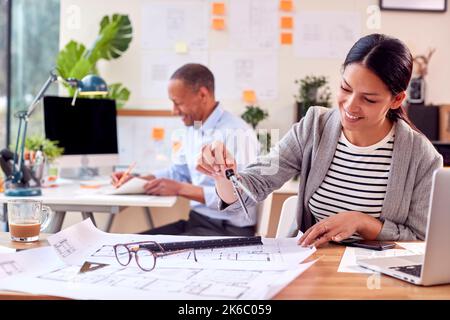 Male And Female Architects Working In Office At Desks On Plans For New Building Stock Photo