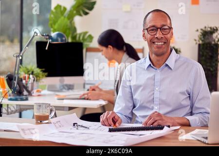 Portrait Of Male And Female Architects Working In Office At Desks On Plans For New Building Stock Photo