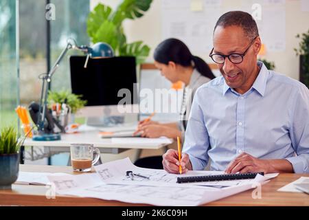 Male And Female Architects Working In Office At Desks On Plans For New Building Stock Photo