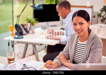 Portrait Of Male And Female Architects Working In Office At Desks On Plans For New Building Stock Photo