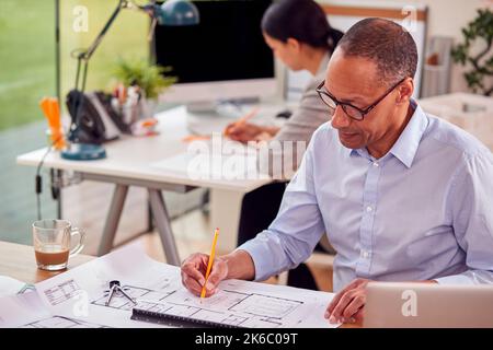 Male And Female Architects Working In Office At Desks On Plans For New Building Stock Photo