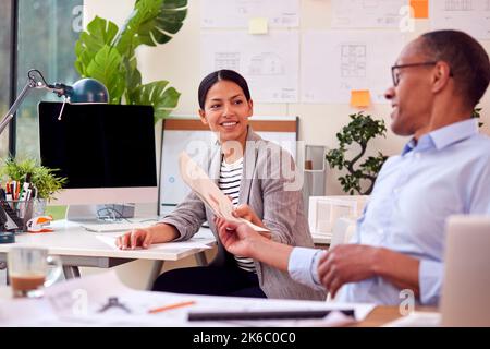 Male And Female Architects Working In Office At Desks Discussing Document On New Building Stock Photo