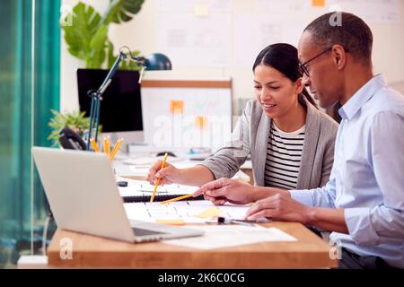 Male And Female Architects Working Together In Office At Desks On Plans For New Building Stock Photo
