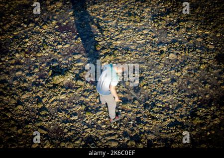 A male metal detectorist searches for long lost items in the late afternoon at low tide on Worthing beach, West Sussex, UK. Stock Photo