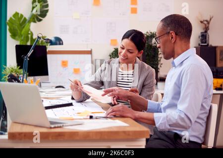 Male And Female Architects Or Interior Designers Working In Office On Plans For New Building Stock Photo
