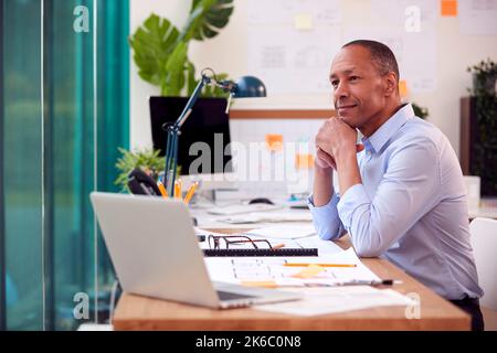 Mature Male Architect Working In Office At Desk Working On Plans For New Building Stock Photo