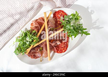 Meat gastronomy. Appetizers with different antipasti, prosciutto crudo, bresaola, Napoli Piccante salami, grissini, sun-dried tomatoes, capers on whit Stock Photo