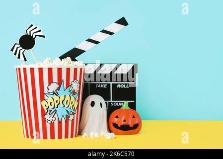 Halloween concept background. Movie clapperboard with popcorn, funny halloween pumpkin and halloween ghost over blue background. Halloween movies conc Stock Photo