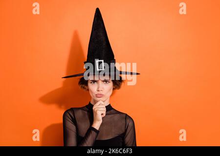 Photo portrait of stunning young woman frowning pensive argument dressed trendy black halloween witch look isolated on orange background Stock Photo