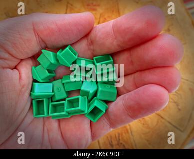 An adult hand, holding green Monopoly houses for rent or by, representing property and UK Housing issues Stock Photo