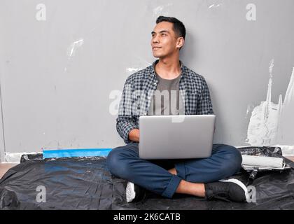 An attractive Asian man sits with laptop researching home DIY ideas and how-to Stock Photo