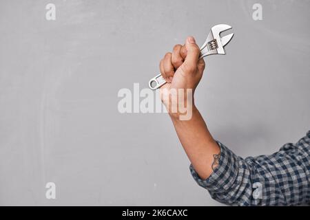 Cropped close up shot of hand holding spanner or wrench against grey wall Stock Photo