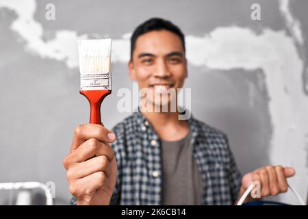Close up selective focus on paintbrush held by attractive Asian man in home DIY Stock Photo