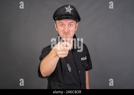 Portrait of Caucasian man wearing police uniform costume against gray studio background Stock Photo