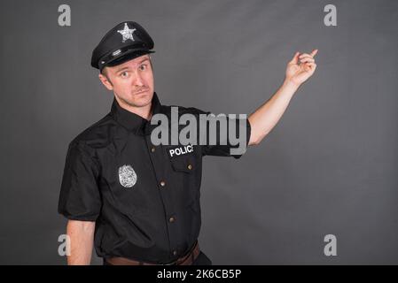 Portrait of Caucasian man wearing police uniform costume against gray studio background Stock Photo