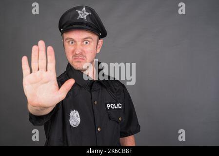 Portrait of Caucasian man wearing police uniform costume against gray studio background Stock Photo