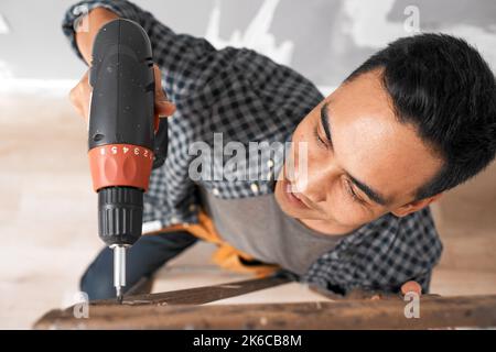 Overhead shot of young Asian man drilling into wood during home renovation Stock Photo